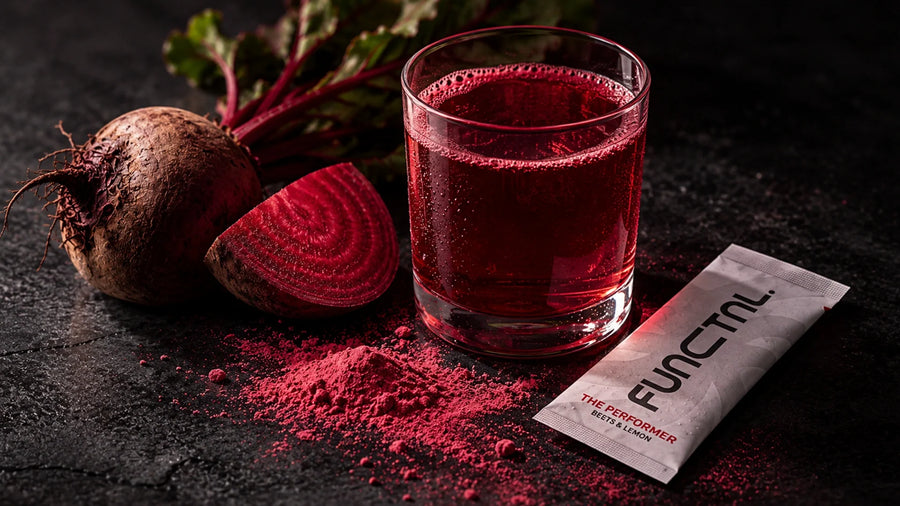 Beetroot-coloured drink in a glass beside fresh beetroot and a sachet of powder